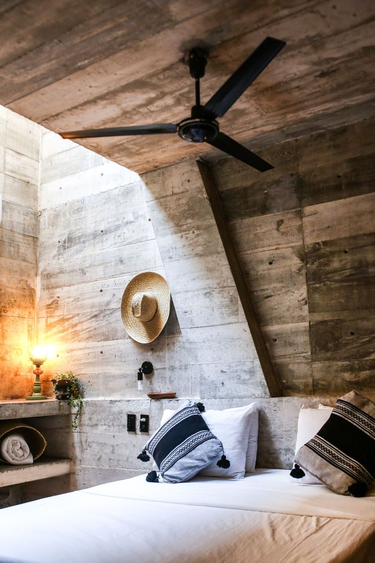 Bedroom under the slanted concrete roof, with a ceiling fan and Oaxacan cushions