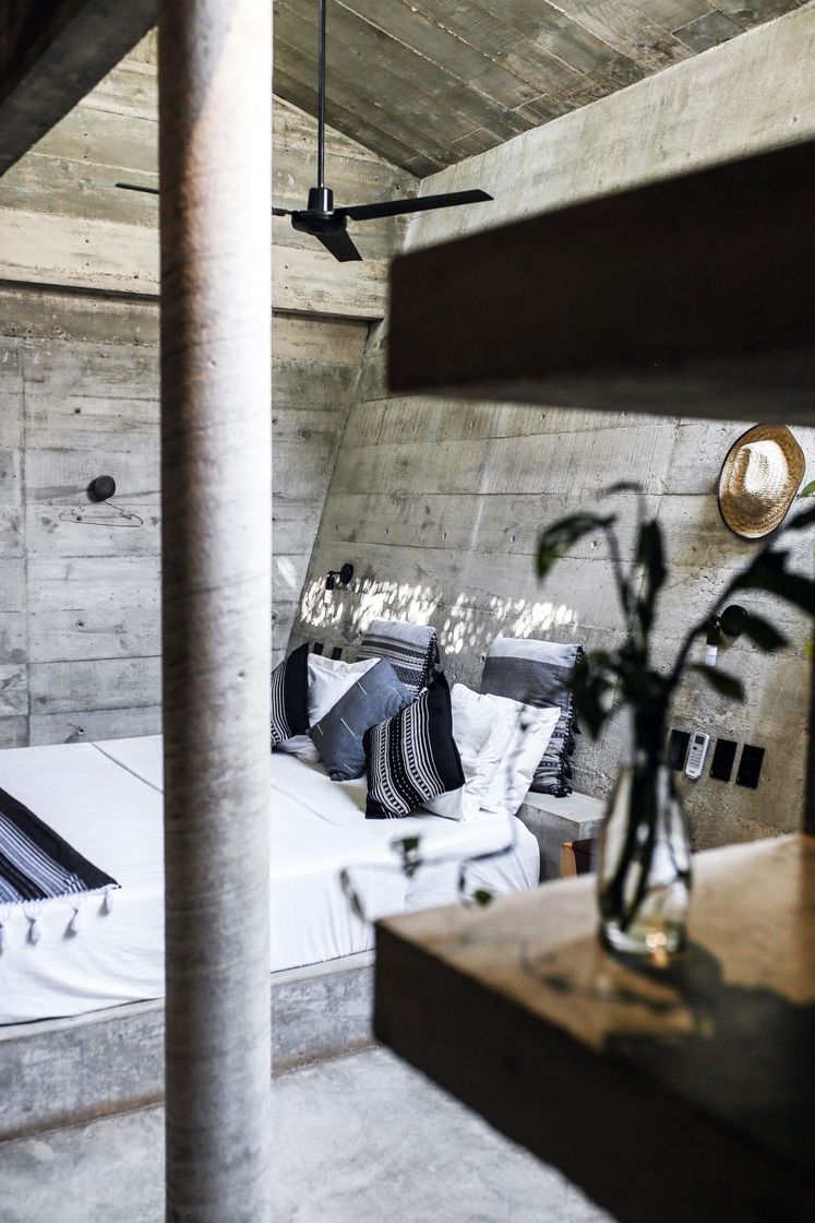 Bed with white linen and striped cushions in a board-formed concrete bedroom
