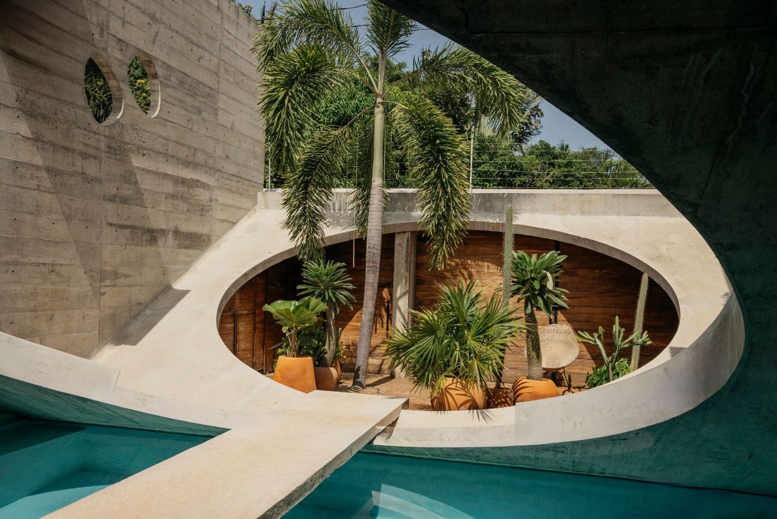 The oval opening with its garden of palms and cacti, the pool and the concrete bridge
