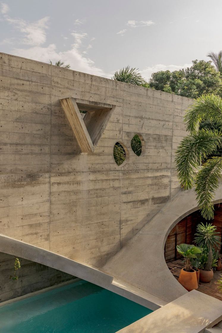 Board-formed concrete wall with a triangular window above the pool
