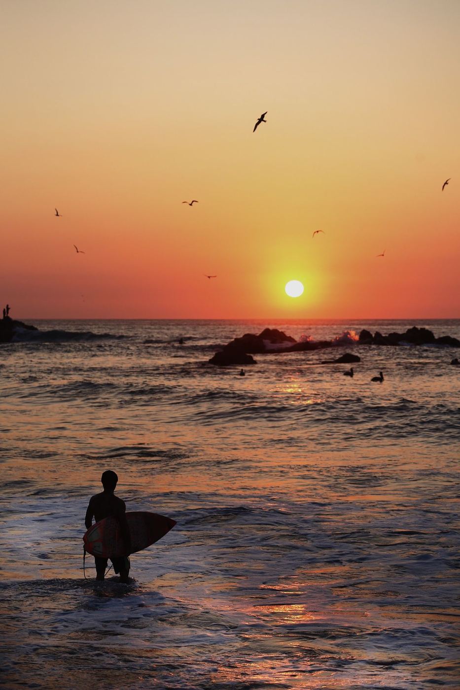 A surfer walking into the sea at sunset in La Punta